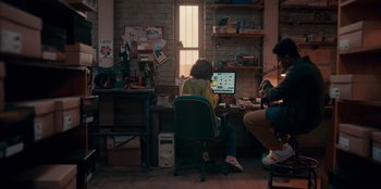 Movie still from “Sneakerella” (2022), directed by Elizabeth Allen Rosenbaum – A couple of people sitting at a table with a laptop; Wide shot, High angle