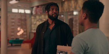 Movie still from “Sneakerella” (2022), directed by Elizabeth Allen Rosenbaum – A man with dreadlocks standing next to another man; Medium shot, Over the shoulder angle