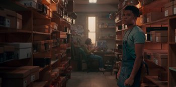 Movie still from “Sneakerella” (2022), directed by Elizabeth Allen Rosenbaum – A man standing in front of shelves in a room; Medium shot, Low angle