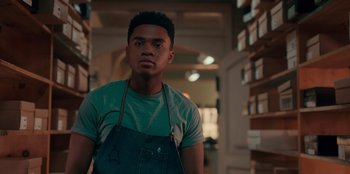 Movie still from “Sneakerella” (2022), directed by Elizabeth Allen Rosenbaum – A man wearing an apron standing in front of shelves; Medium shot, Low angle