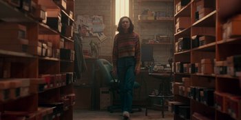 Movie still from “Sneakerella” (2022), directed by Elizabeth Allen Rosenbaum – A person standing in a room with lots of books on the floor; Wide shot, High angle