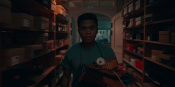 Movie still from “Sneakerella” (2022), directed by Elizabeth Allen Rosenbaum – A man holding a basket in a room filled with shelves; Medium shot, Low angle