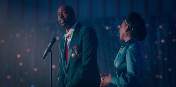 Movie still from “Sneakerella” (2022), directed by Elizabeth Allen Rosenbaum – A man and a woman standing next to a microphone; Medium shot, Over the shoulder angle