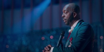 Movie still from “Sneakerella” (2022), directed by Elizabeth Allen Rosenbaum – A man holding a microphone in front of a crowd; Close Up shot, Low angle