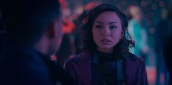 Movie still from “Sneakerella” (2022), directed by Elizabeth Allen Rosenbaum – A young woman wearing a purple jacket and headphones in front of blurry lights; Close Up shot, Over the shoulder angle
