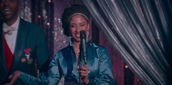 Movie still from “Sneakerella” (2022), directed by Elizabeth Allen Rosenbaum – A woman holding a microphone and smiling at the camera; Close Up shot, Over the shoulder angle