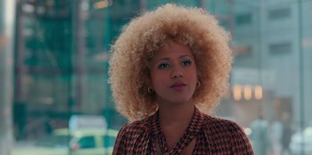 Movie still from “Sneakerella” (2022), directed by Elizabeth Allen Rosenbaum – A woman with blonde afro hair standing in front of a building; Close Up shot, Over the shoulder angle