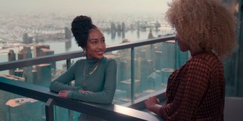 Two women are sitting on a balcony overlooking a city