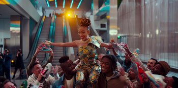 Movie still from “Sneakerella” (2022), directed by Elizabeth Allen Rosenbaum – A group of people sitting and standing around a woman in a dress; Medium shot, Low angle