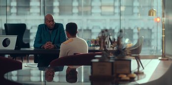 Movie still from “Sneakerella” (2022), directed by Elizabeth Allen Rosenbaum – Two men sitting at a table in front of each other; Medium shot, Over the shoulder angle