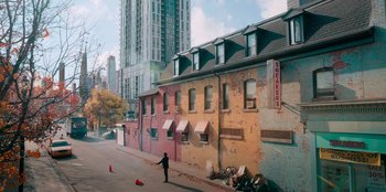 Movie still from “Sneakerella” (2022), directed by Elizabeth Allen Rosenbaum – A person standing on the side of the road near some buildings; Extreme Wide shot, High angle