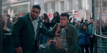 Movie still from “Sneakerella” (2022), directed by Elizabeth Allen Rosenbaum – Two men are standing in front of a group of people; Medium shot, Over the shoulder angle