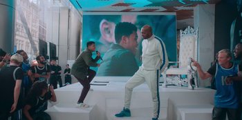 Movie still from “Sneakerella” (2022), directed by Elizabeth Allen Rosenbaum – Two men are posing in front of a large screen; Wide shot, Over the shoulder angle