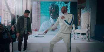 Movie still from “Sneakerella” (2022), directed by Elizabeth Allen Rosenbaum – A man standing in front of a large screen; Medium shot, Low angle