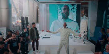 Movie still from “Sneakerella” (2022), directed by Elizabeth Allen Rosenbaum – Two men are standing in front of a large screen; Medium shot, Over the shoulder angle