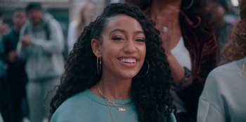 Movie still from “Sneakerella” (2022), directed by Elizabeth Allen Rosenbaum – A person with curly hair smiling; Close Up shot, Over the shoulder angle