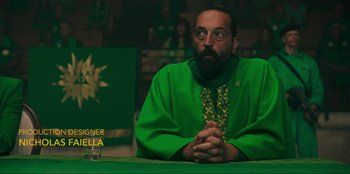 Movie still from “Sniper: G.R.I.T. - Global Response & Intelligence Team” (2023), directed by Oliver Thompson – A man sitting at a table with his hands clasped together; Medium shot, Low angle