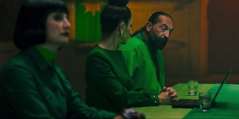 Movie still from “Sniper: G.R.I.T. - Global Response & Intelligence Team” (2023), directed by Oliver Thompson – A man and woman sitting at a table with another man; Medium shot, Over the shoulder angle