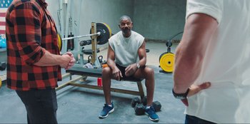 Movie still from “Sniper: G.R.I.T. - Global Response & Intelligence Team” (2023), directed by Oliver Thompson – A man sitting on a bench in a gym; Wide shot, Over the shoulder angle