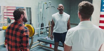 Movie still from “Sniper: G.R.I.T. - Global Response & Intelligence Team” (2023), directed by Oliver Thompson – A man standing next to a bench in a gym; Wide shot, Over the shoulder angle