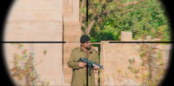 Movie still from “Sniper: G.R.I.T. - Global Response & Intelligence Team” (2023), directed by Oliver Thompson – A man holding a rifle in front of a brick wall; Wide shot, Over the shoulder angle