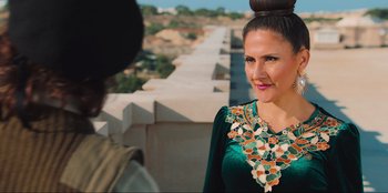 Movie still from “Sniper: G.R.I.T. - Global Response & Intelligence Team” (2023), directed by Oliver Thompson – A woman in a green dress standing next to a wall; Medium shot, Over the shoulder angle