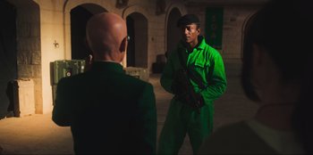 Movie still from “Sniper: G.R.I.T. - Global Response & Intelligence Team” (2023), directed by Oliver Thompson – A man in a green suit is holding a gun; Medium shot, Over the shoulder angle