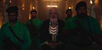 Movie still from “Sniper: G.R.I.T. - Global Response & Intelligence Team” (2023), directed by Oliver Thompson – A man with a long white beard is holding a sword in front of a group of men; Medium shot, Low angle
