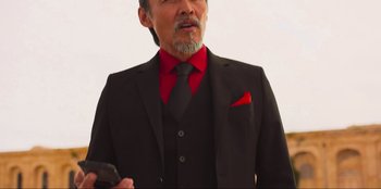 Movie still from “Sniper: G.R.I.T. - Global Response & Intelligence Team” (2023), directed by Oliver Thompson – A man in a suit and tie holding a cell phone; Close Up shot, Low angle