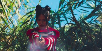 Movie still from “Sniper: G.R.I.T. - Global Response & Intelligence Team” (2023), directed by Oliver Thompson – A young girl holding a gun in her hands; Medium shot, Low angle