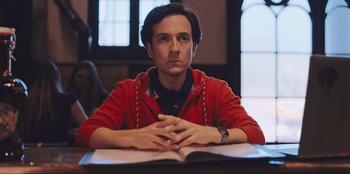 Movie still from “Sniper: G.R.I.T. - Global Response & Intelligence Team” (2023), directed by Oliver Thompson – A man sitting at a table in front of an open book; Medium shot, Low angle