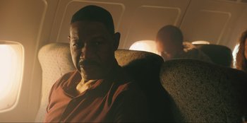Movie still from “Sniper: G.R.I.T. - Global Response & Intelligence Team” (2023), directed by Oliver Thompson – A man sitting on a seat on an airplane; Close Up shot, Over the shoulder angle