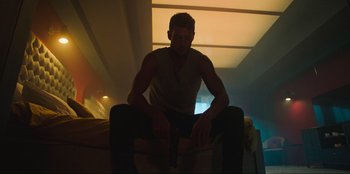 Movie still from “Sniper: G.R.I.T. - Global Response & Intelligence Team” (2023), directed by Oliver Thompson – A man sitting on top of a chair in a room; Medium shot, Low angle