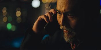 Movie still from “Sniper: G.R.I.T. - Global Response & Intelligence Team” (2023), directed by Oliver Thompson – A person talking on a cell phone; Close Up shot, Low angle
