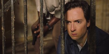 Movie still from “Sniper: G.R.I.T. - Global Response & Intelligence Team” (2023), directed by Oliver Thompson – A man with a gun behind bars in a jail cell; Close Up shot, High angle