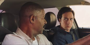 Movie still from “Sniper: G.R.I.T. - Global Response & Intelligence Team” (2023), directed by Oliver Thompson – Two men sitting in the back seat of a car; Close Up shot, Over the shoulder angle