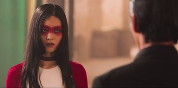 Movie still from “Sniper: G.R.I.T. - Global Response & Intelligence Team” (2023), directed by Oliver Thompson – A woman with a red face paint standing in front of a man; Close Up shot, Over the shoulder angle