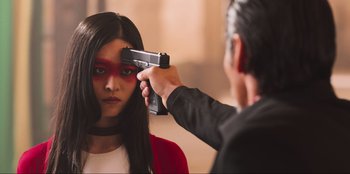 Movie still from “Sniper: G.R.I.T. - Global Response & Intelligence Team” (2023), directed by Oliver Thompson – A woman getting her hair cut by a man with a gun pointed at her face; Close Up shot, Over the shoulder angle