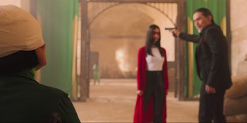 Movie still from “Sniper: G.R.I.T. - Global Response & Intelligence Team” (2023), directed by Oliver Thompson – A person holding a gun in front of a woman; Medium shot, Over the shoulder angle