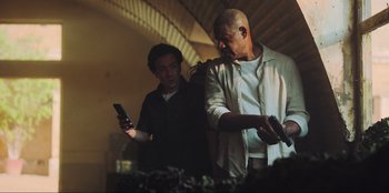 Movie still from “Sniper: G.R.I.T. - Global Response & Intelligence Team” (2023), directed by Oliver Thompson – Two men standing next to each other holding cell phones; Medium shot, Low angle