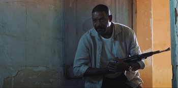 Movie still from “Sniper: G.R.I.T. - Global Response & Intelligence Team” (2023), directed by Oliver Thompson – A man holding a cell phone while standing next to a wall; Medium shot, Low angle