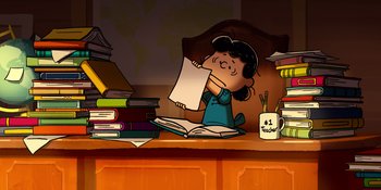 Movie still from “Snoopy Presents: Lucy's School” (2022), directed by Raymond S. Persi – A girl is sitting at a desk holding a sheet of paper in front of her face; Medium shot, High angle