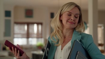 Movie still from “Snow Day” (2022), directed by Michael Lembeck – A woman holding a folder and smiling at the camera; Medium shot, Over the shoulder angle