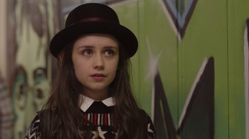 Movie still from “Snow Day” (2022), directed by Michael Lembeck – A young girl wearing a black hat and a black tie; Close Up shot, Over the shoulder angle