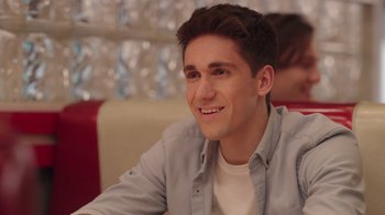 Movie still from “Snow Day” (2022), directed by Michael Lembeck – A man sitting in front of a window smiling for the camera; Close Up shot, Over the shoulder angle