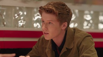 Movie still from “Snow Day” (2022), directed by Michael Lembeck – A young man sitting in front of a red wall; Close Up shot, Over the shoulder angle