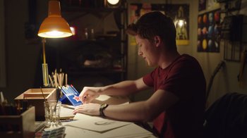Movie still from “Snow Day” (2022), directed by Michael Lembeck – A man sitting at a table looking at an item in a box; Medium shot, Low angle