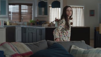 Movie still from “Snow Day” (2022), directed by Michael Lembeck – A young girl in pajamas standing on top of a couch; Medium shot, Over the shoulder angle