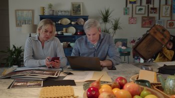 Movie still from “Snow Day” (2022), directed by Michael Lembeck – A man and a woman sitting at a table looking at a computer; Medium shot, High angle