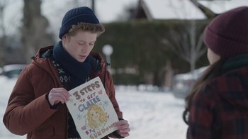 Movie still from “Snow Day” (2022), directed by Michael Lembeck – A young man holding a sign that says " 3 steps to get class "; Close Up shot, Over the shoulder angle